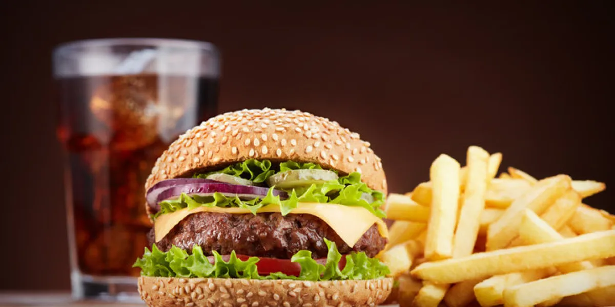 fresh cheeseburger with glass of cola and pile of french fries on wooden table