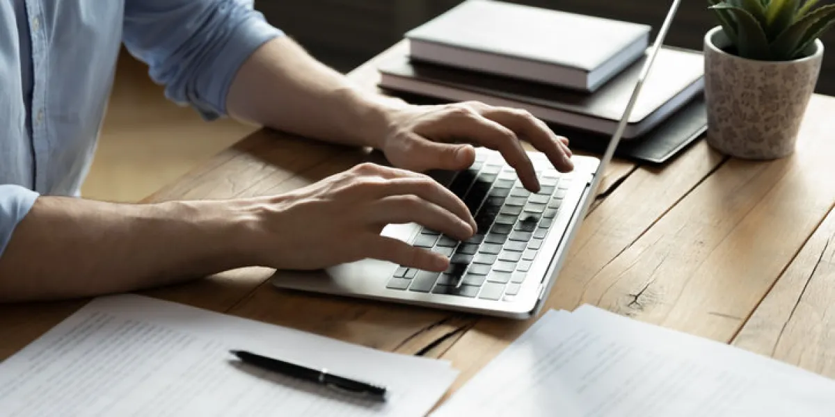 close up businessman using laptop, typing on keyboard, sitting at wooden desk with documents, writing email, accountant writing financial report, busy student studying online, searching information
