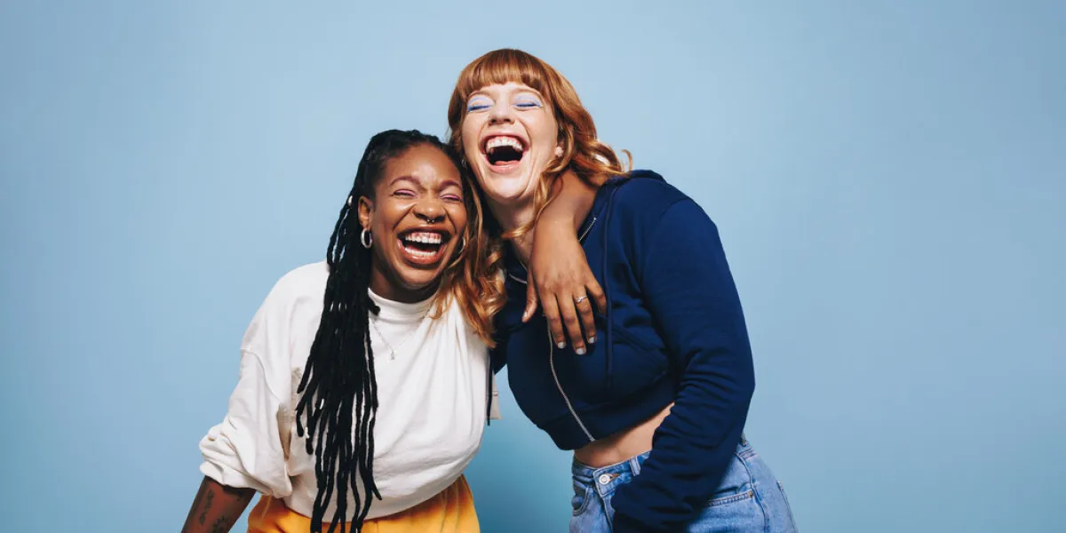 interracial best friends laughing and having a good time together in a studio happy young women enjoying themselves while standing against a blue background two vibrant female friends making memories interracial best friends laughing and having a good time together in a studio happy young women enjoying themselves while standing against a blue background two vibrant female friends making memories