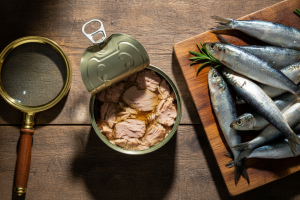 Hyper-realistic top-down shot on a rustic wooden kitchen table. An open tin of tuna fish in the cent