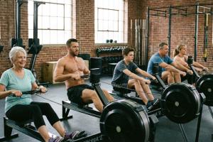 Dans une salle de gym, une série de personnes de tous âges en train de pratiquer du rameur