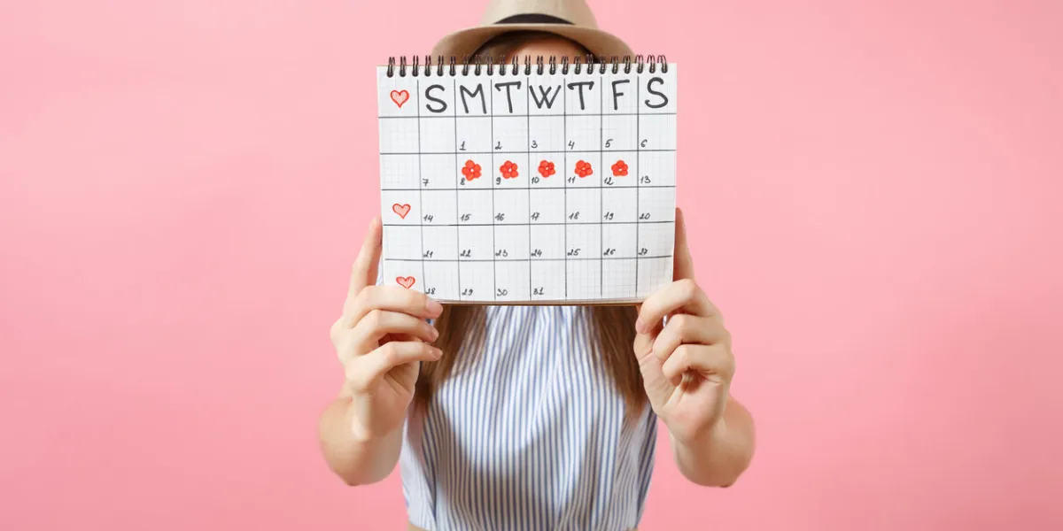 portrait of woman in blue dress cover face, hiding behind periods calendar for checking menstruation days isolated on trending pink background medical, healthcare, gynecological concept copy space