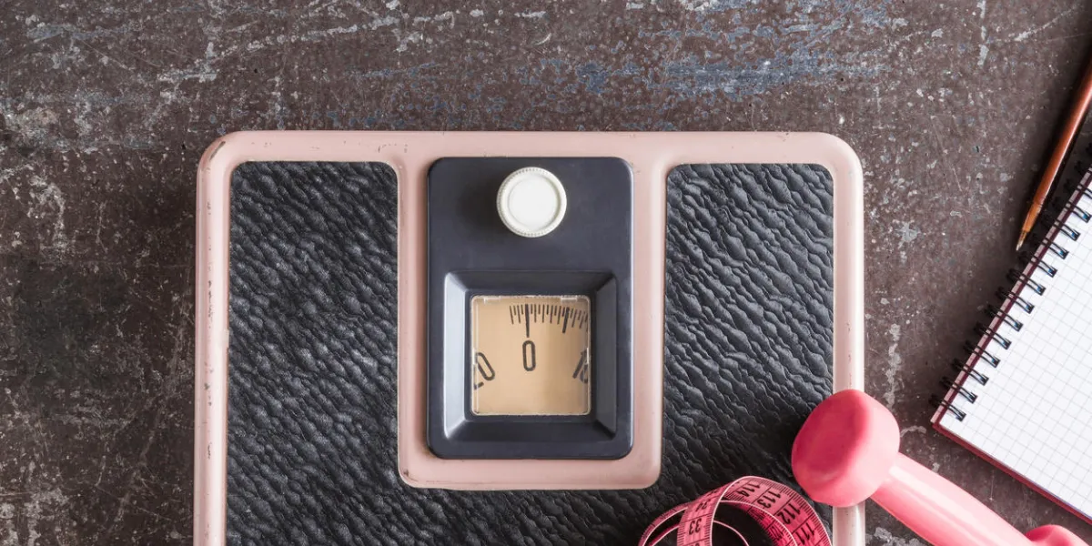 old weight scale, dumbbell, measuring tape and notebook on the dark floor in the gym cares about a body weight loss concept top view