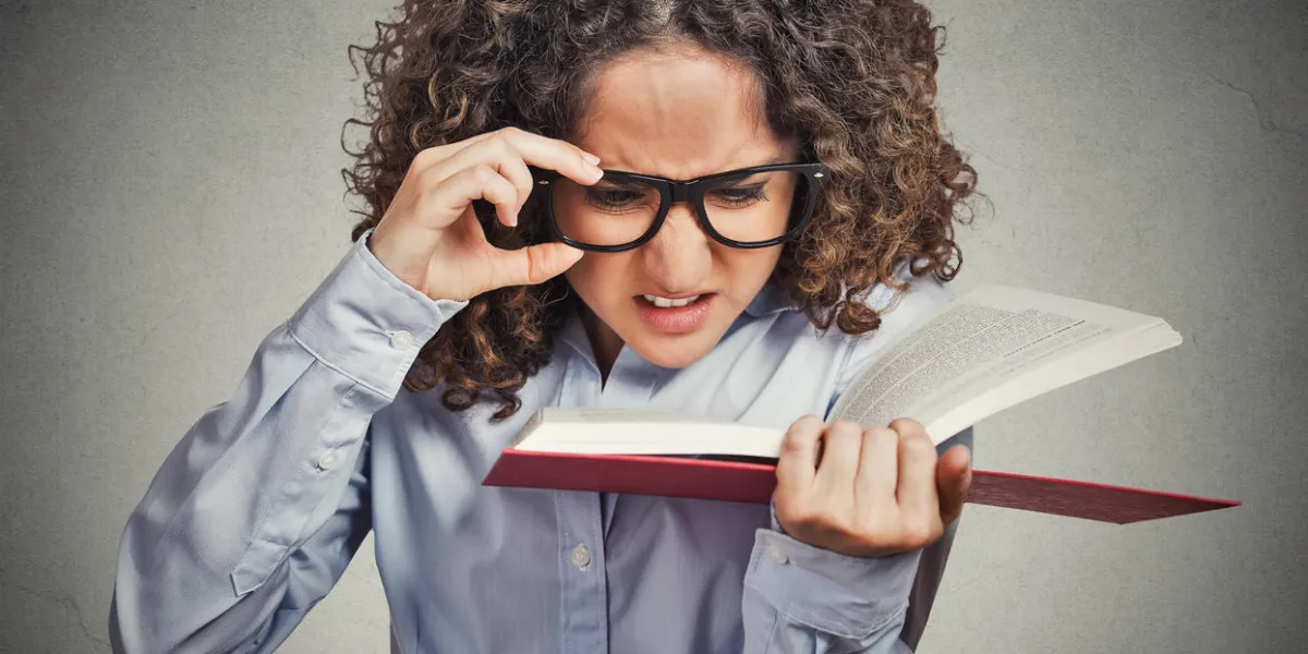 closeup portrait young woman with eye glasses trying to read book, having difficulties seeing text, bad vision sight problem isolated grey background face expression reaction health eyesight issues closeup portrait young woman with eye glasses trying to read book, having difficulties seeing text, bad vision sight problem isolated grey background face expression reaction health eyesight issues