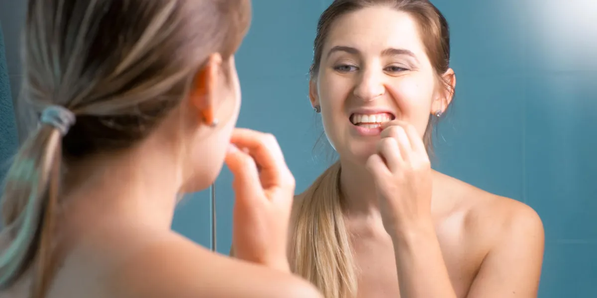 portrait of young woman checking her teeth at mirror portrait of young woman checking her teeth at mirror