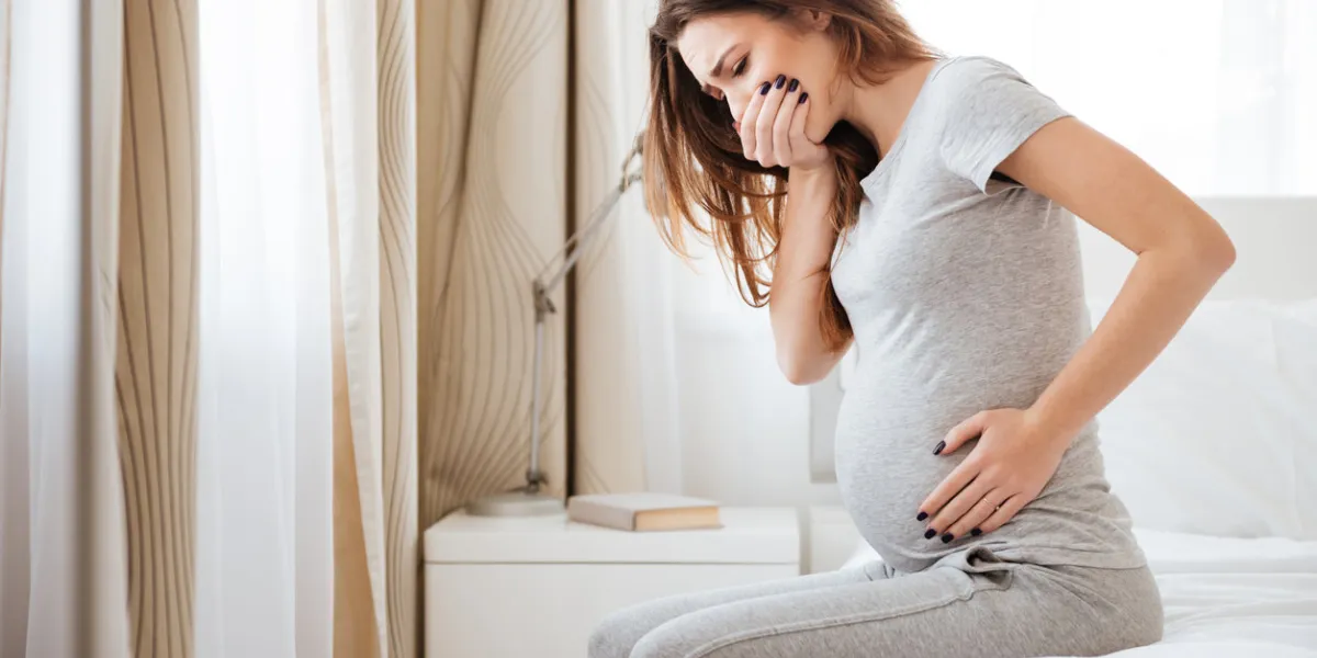 pregnant young woman sitting on bed and feeling sick