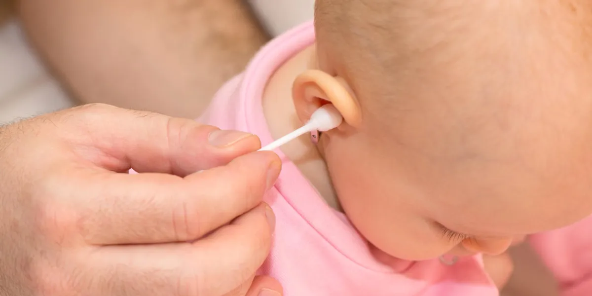 father cleaning baby's ear withj a cotton bud