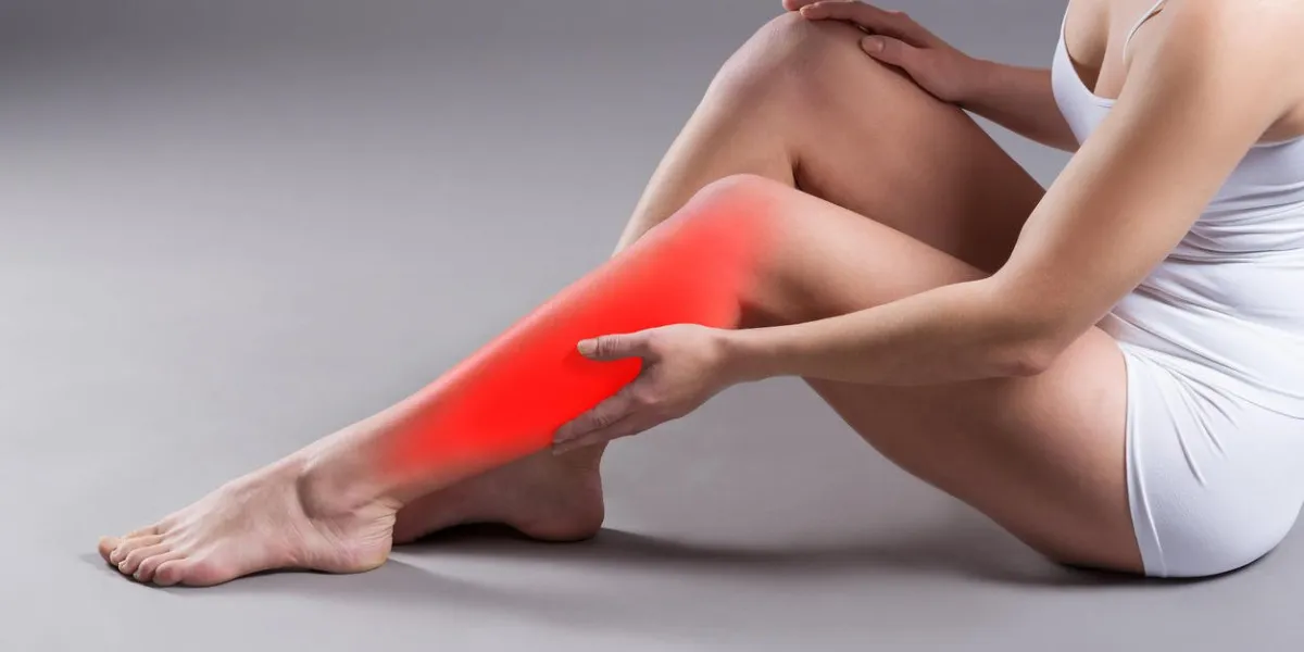 pain in woman's shin, massage of female leg on gray background, studio shot with red dot