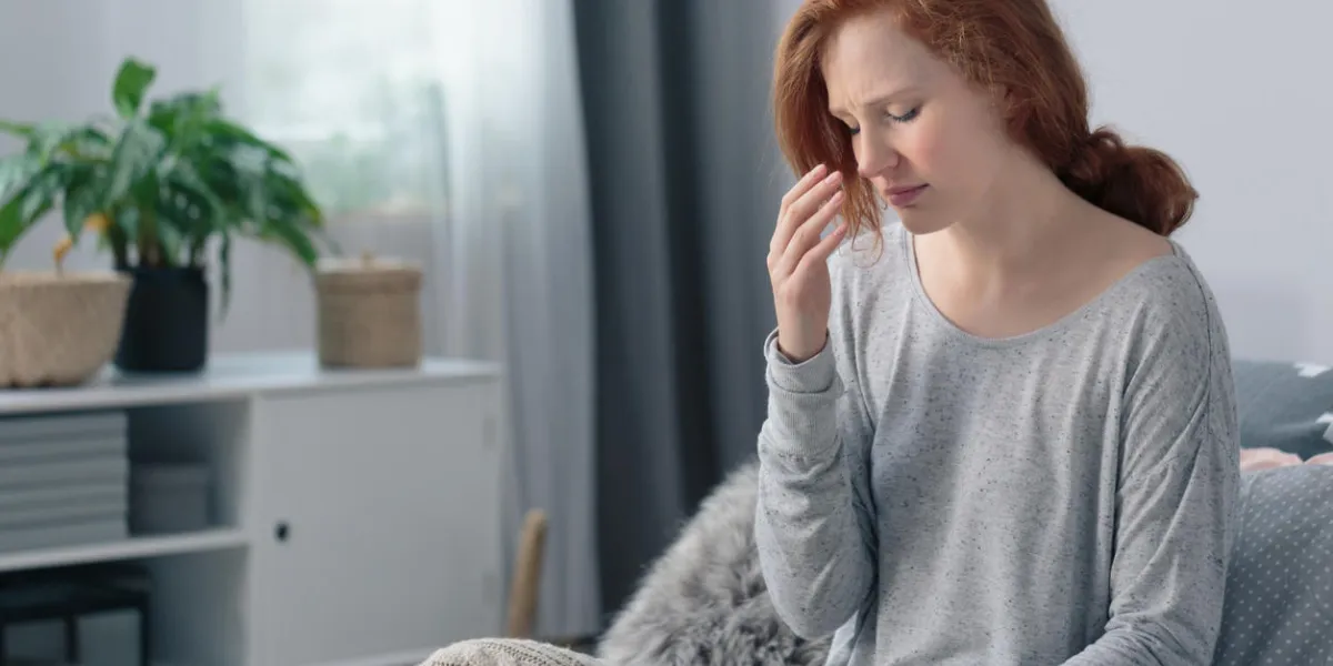 young woman sick with flu having headache sitting on the bed suffering from runny nose and high fever