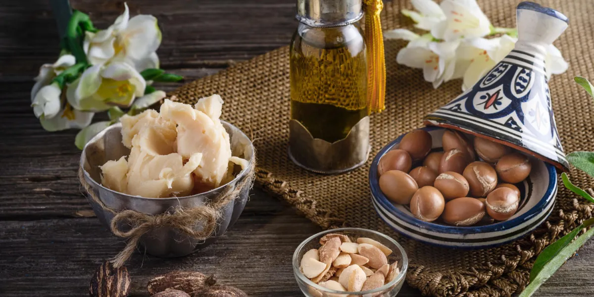nature morte d'huile d'argan et de fruits et de beurre de karité avec des noix sur une table en bois avec des fleurs
