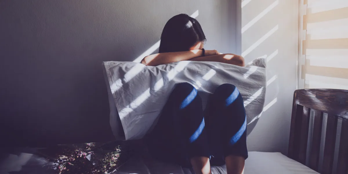 asian women are sitting hugging their knees in bed feeling sad, disappointed in love in the dark bedroom and sunlight from the window through the blindsvintage tone