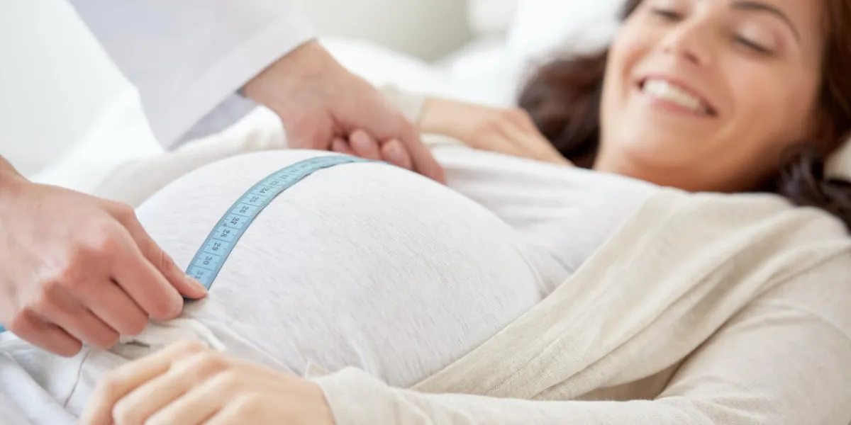 pregnancy, medicine, health care and people concept - close up of obstetrician doctor with centimeter tape measuring pregnant woman tummy at hospital