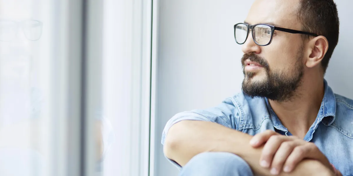 homme calme en chemise denim et lunettes à la recherche à travers la fenêtre