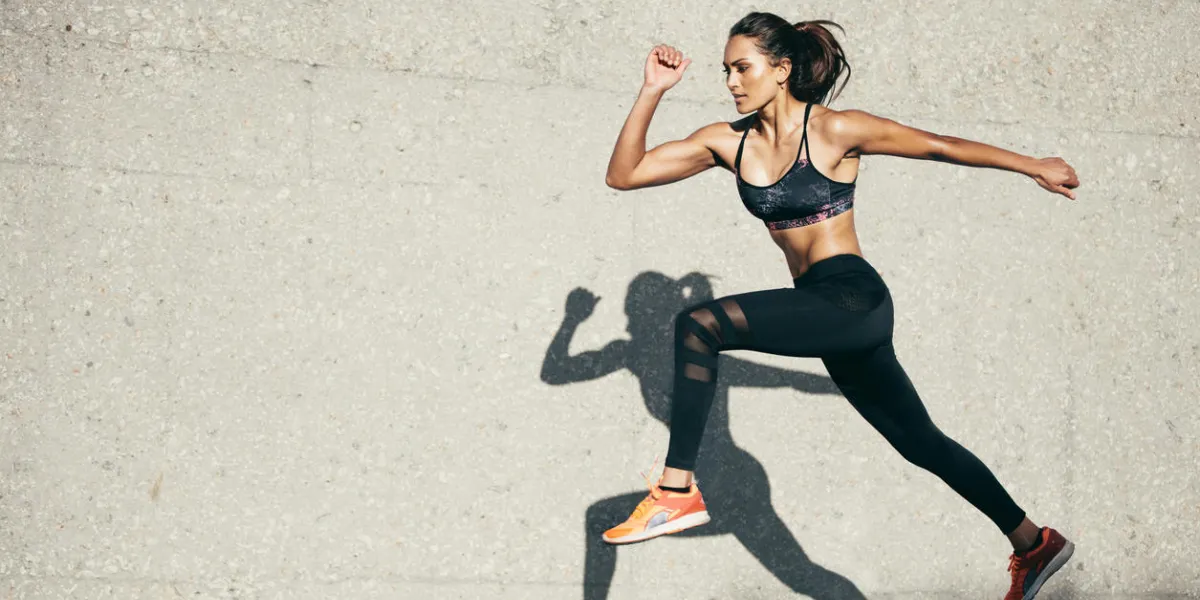 young woman with fit body jumping and running against grey background female model in sportswear exercising outdoors young woman with fit body jumping and running against grey background female model in sportswear exercising outdoors