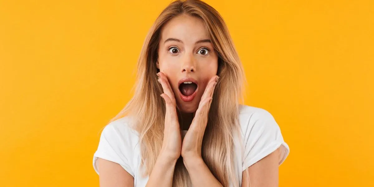 portrait of a surprised young blonde girl looking at camera isolated over yellow background