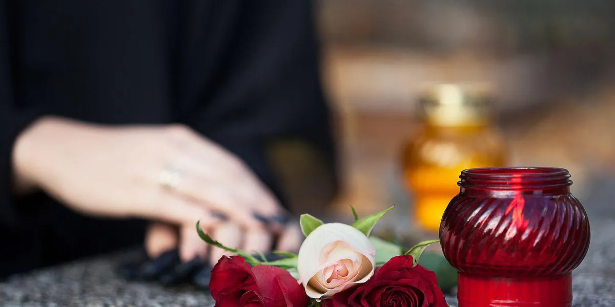 femme en deuil arrangeant des fleurs et des bougies sur la pierre tombale