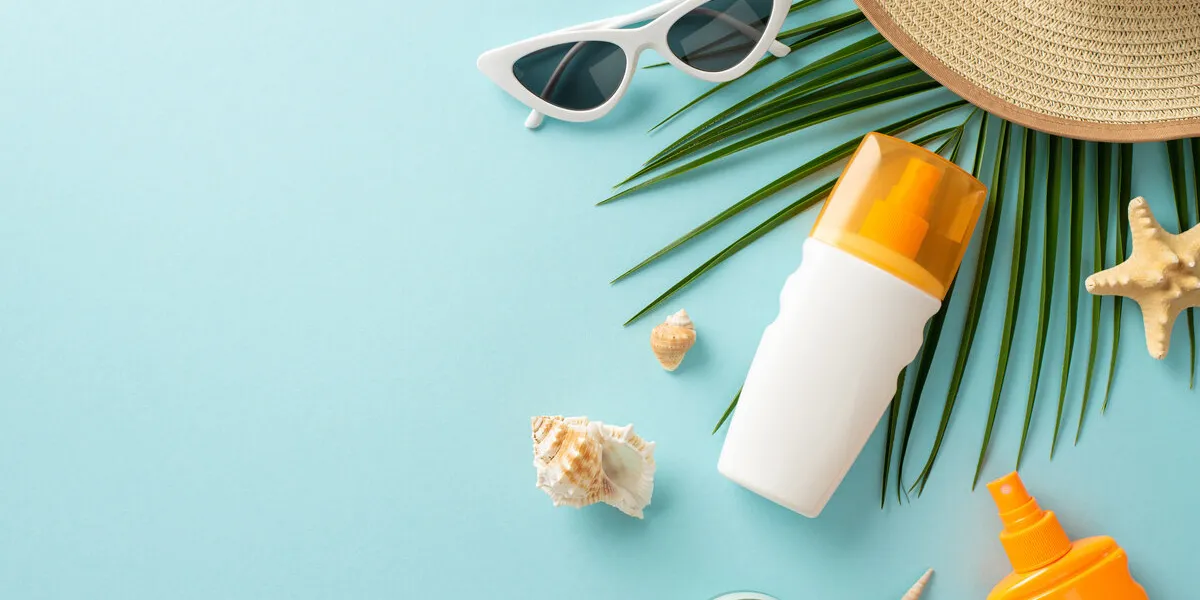 uv safety awareness month high angle view photo of sun protection lotion, sunglasses, straw hat and marine shells with palm leaf on light blue isolated background with copy-space