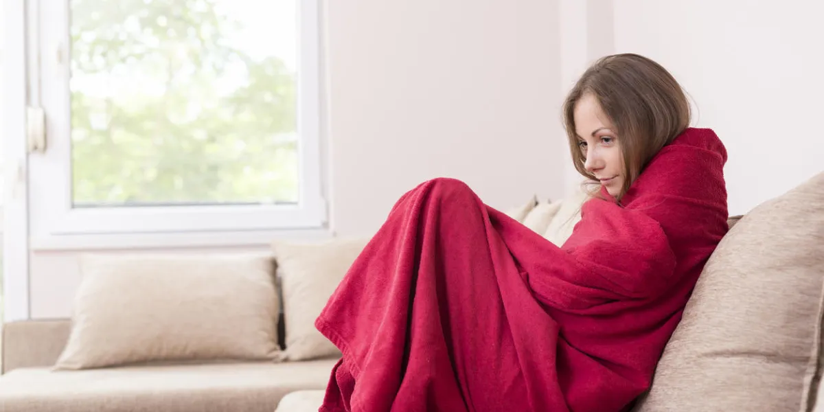 young woman sitting on a couch covered with blanket, having a fever young woman sitting on a couch covered with blanket, having a fever