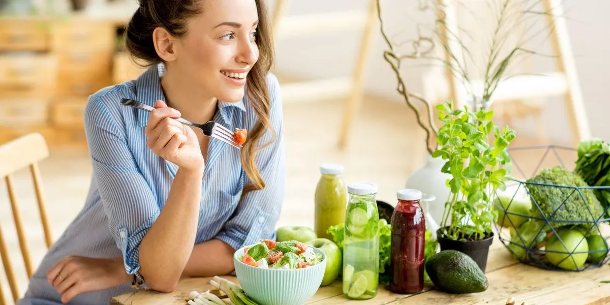 femme jeune et heureuse, manger une salade saine assis sur la table avec des ingrédients frais verts à l'intérieur
