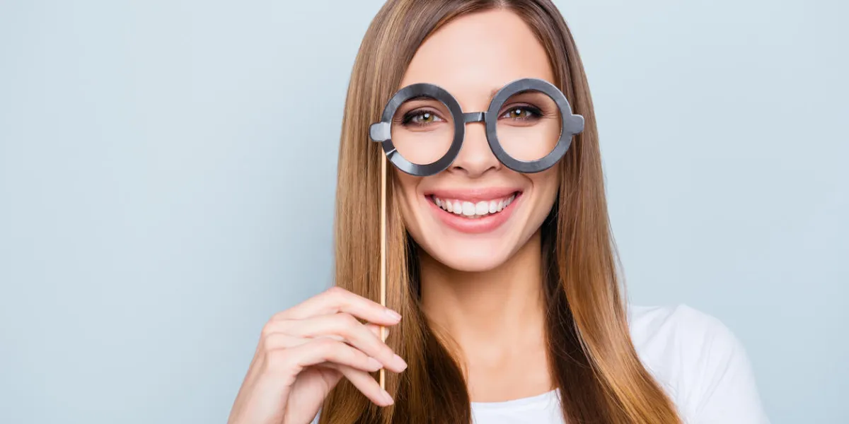 close up portrait of playful positive girl holding black carton glasses on stick looking at camera isolated on grey background