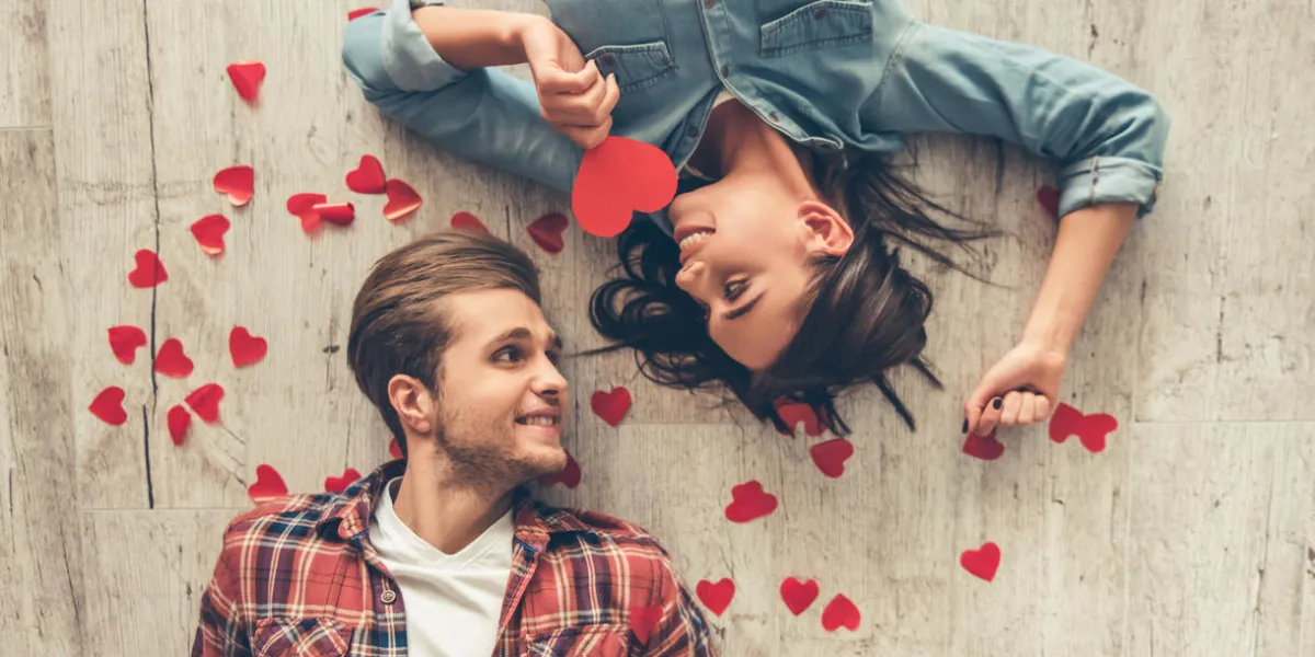 top view of happy young couple looking at each other and smiling while lying on wooden floor girl is holding a red paper heart top view of happy young couple looking at each other and smiling while lying on wooden floor girl is holding a red paper heart