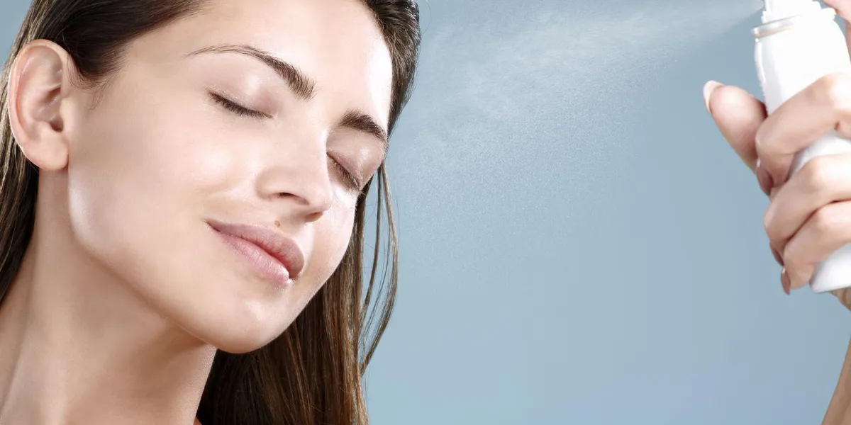 belle femme, appliquer le traitement de l'eau de pulvérisation sur le visage sur fond bleu