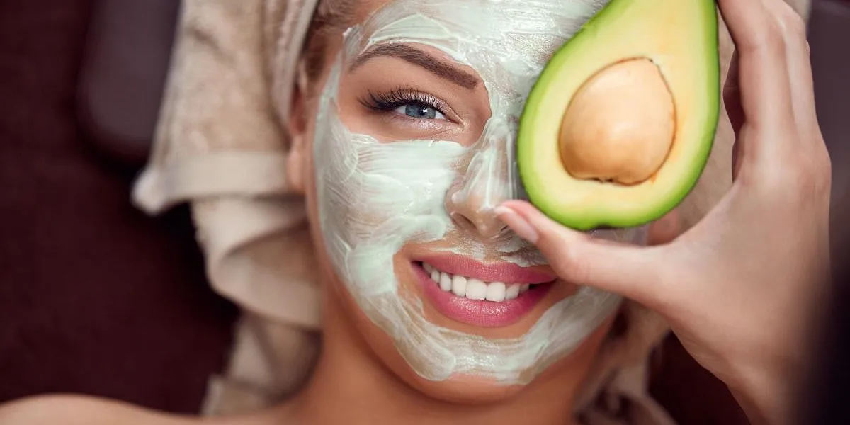 portrait of a young woman applying natural avocado mask on her face