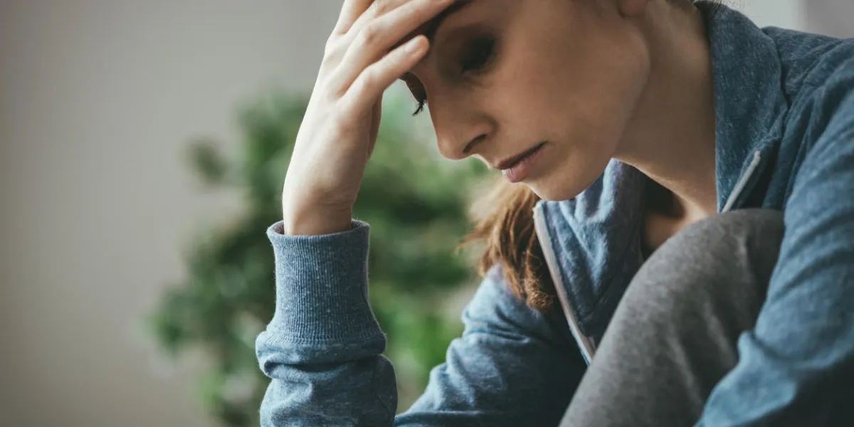 sad depressed woman at home sitting on the couch, looking down and touching her forehead, loneliness and pain concept