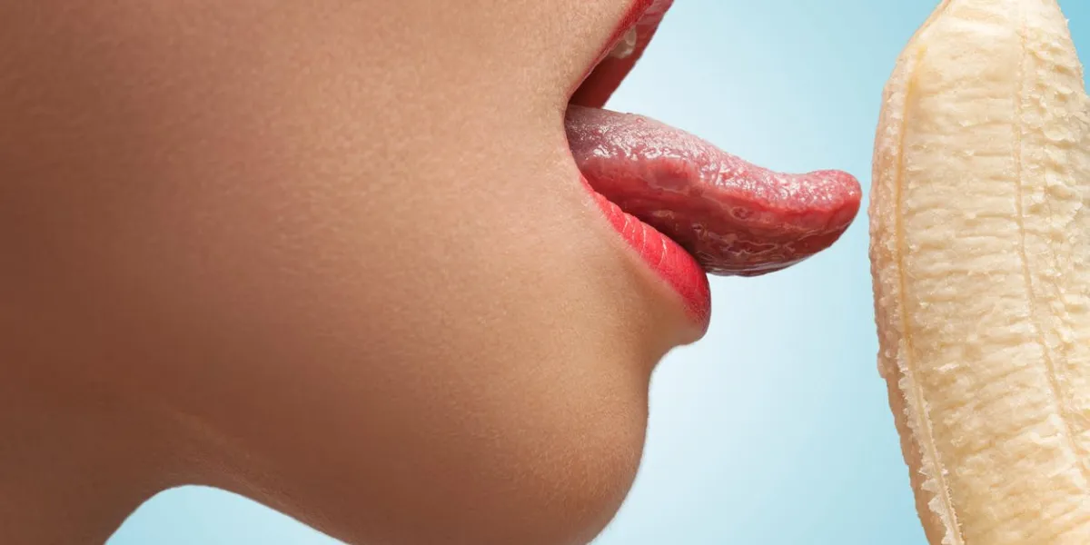 a face of a hot girl that is licking a half-peeled yellow banana