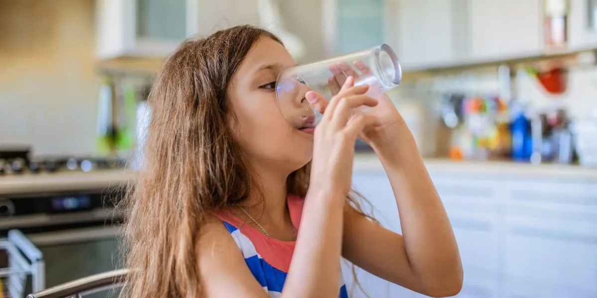 little beautiful happy girl drinking a glass of water in the kitchen