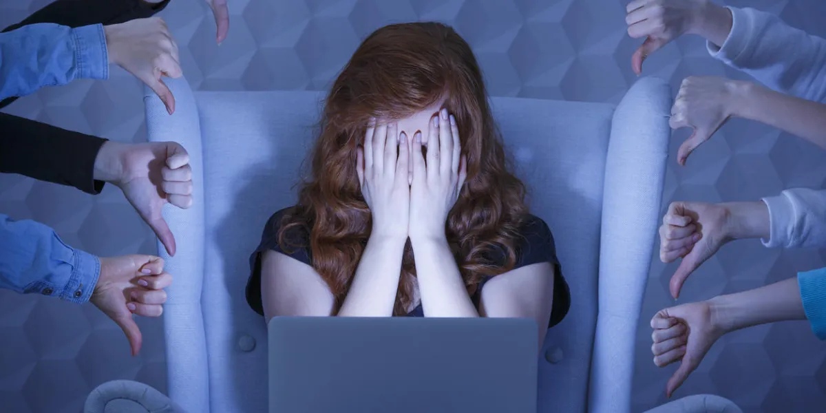 girl with laptop covering face, around hands holding thumbs down