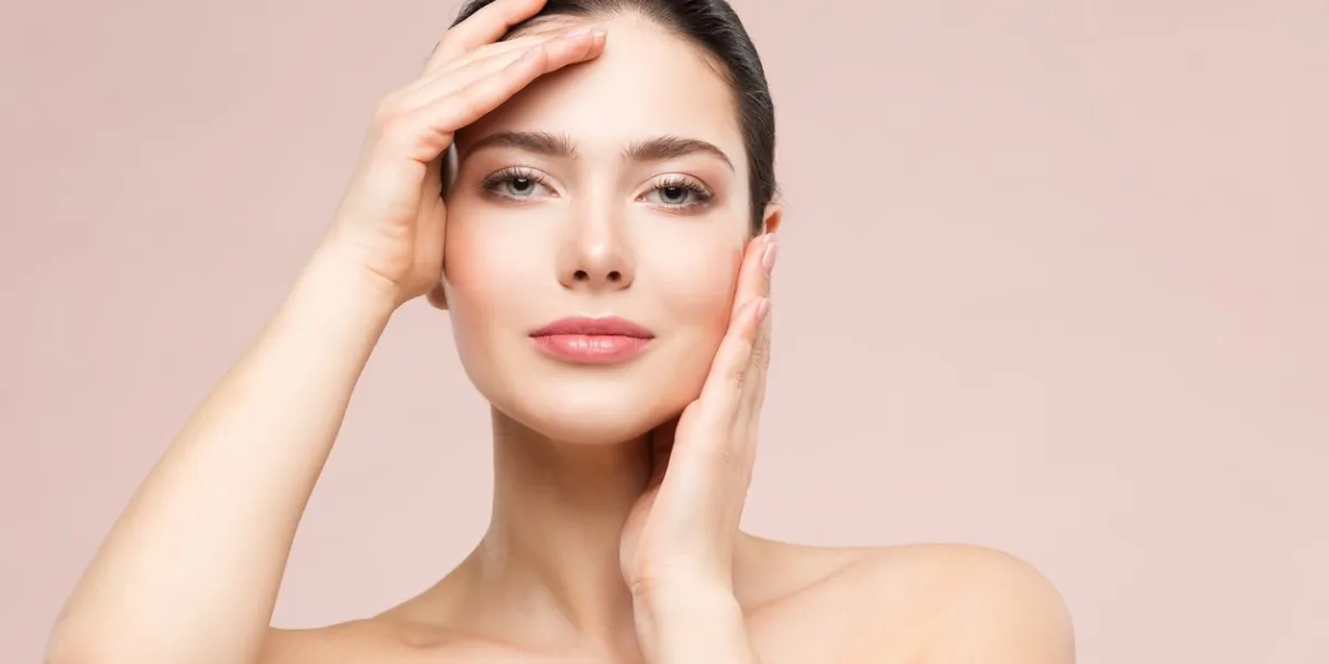 woman natural beauty makeup portrait, fashion model touching face by hands, beautiful girl skin care and treatment, shot over beige studio background