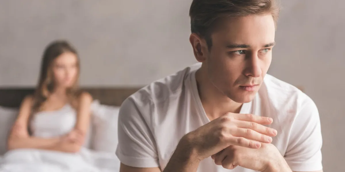 jeune couple ayant un problème gars est assis sur le lit et regardant tristement loin, sa petite amie en arrière-plan