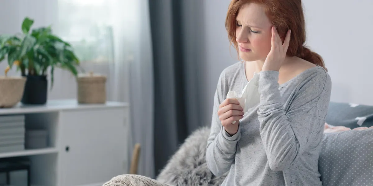 sick young woman with headache and fever sitting with blanket on bed