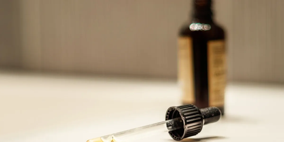 transparent glass dropper with liquid spilled on a surface with a brown bottle as a blur background transparent glass dropper with liquid spilled on a surface with a brown bottle as a blur background