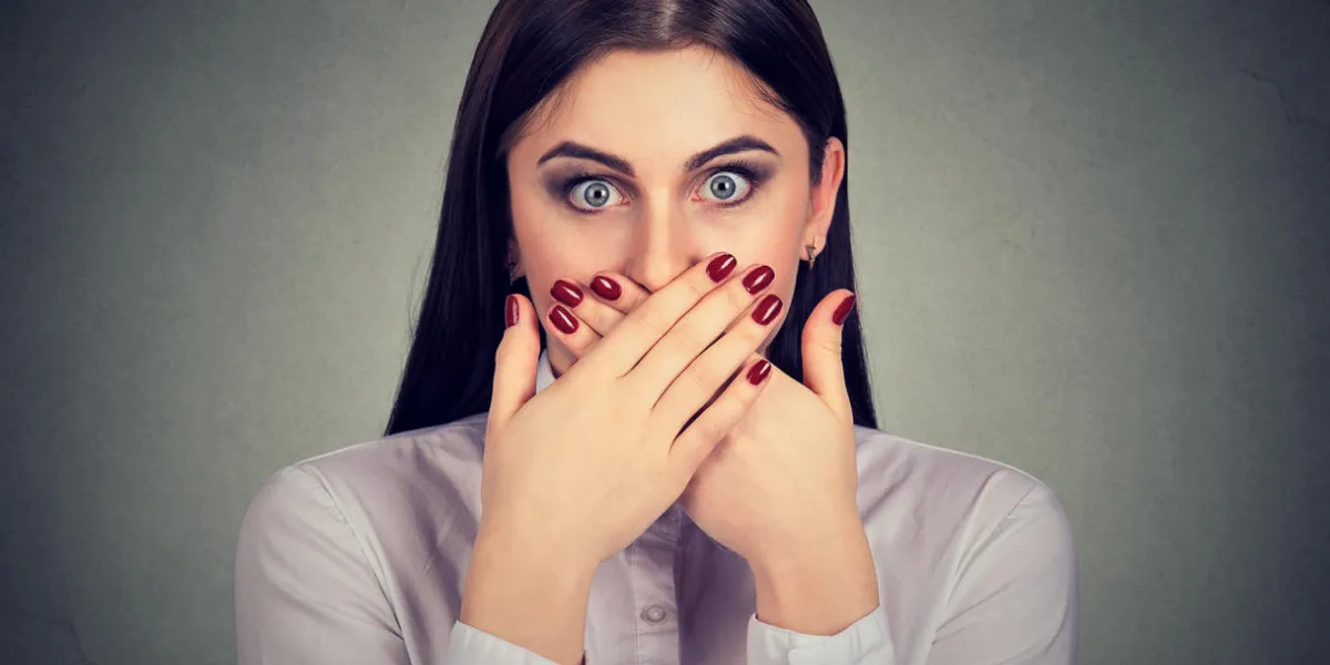 young woman covering mouth looking terrified because of prohibition to talk