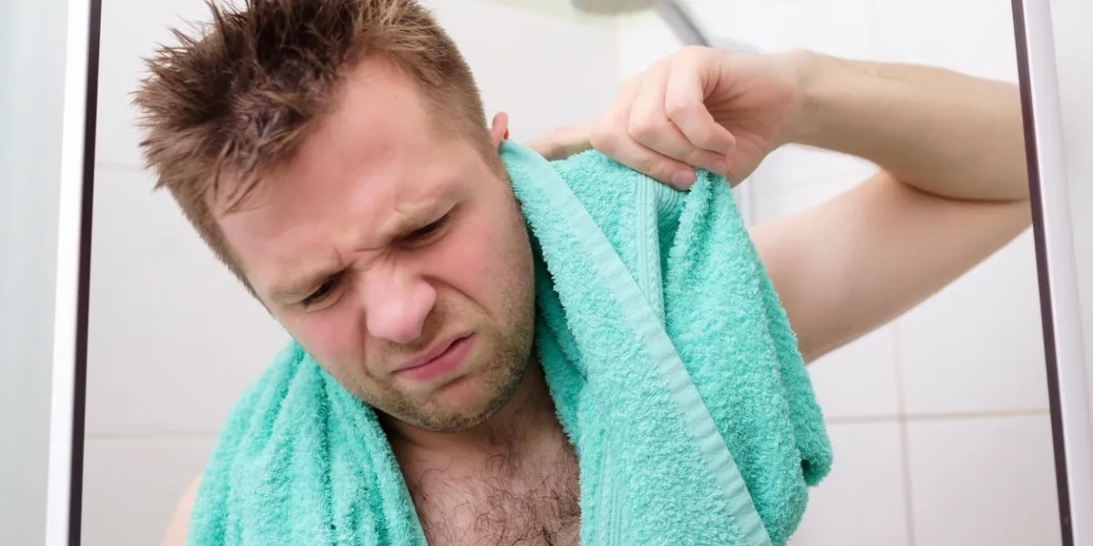 young caucasian man cleaning his ear while taking a shower and standing under flowing water young caucasian man cleaning his ear while taking a shower and standing under flowing water