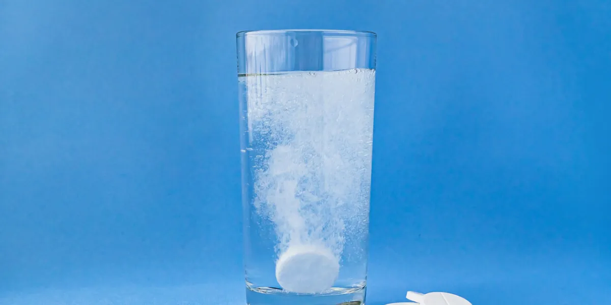fizzy aspirin in a glass of water on a blue background vertical