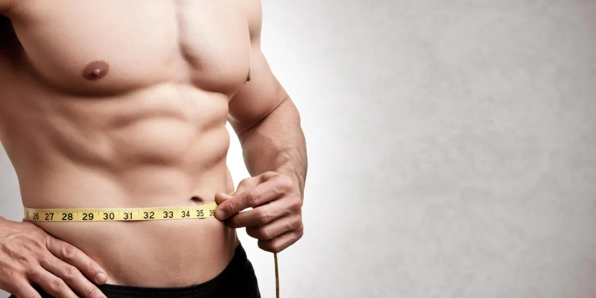 fit man measuring his waist after a workout in the gym, isolated in a grey background