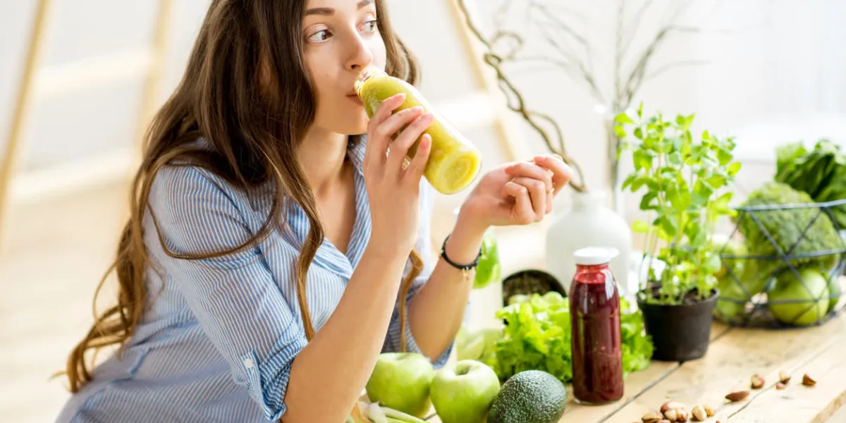 beautiful woman sitting with healthy green food and drinking smoothie at home vegan meal and detox concept