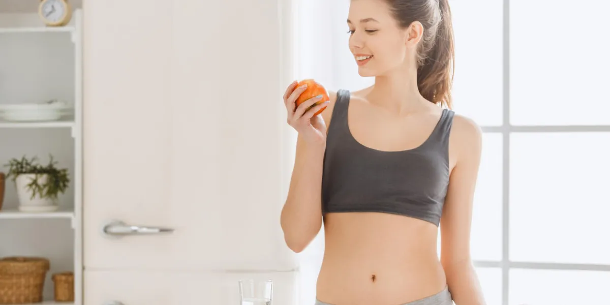 young female weight loss standing in the kitchen eating apple