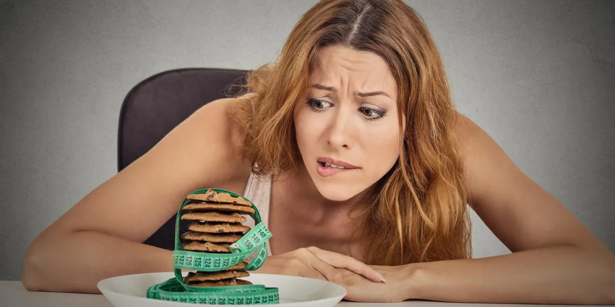 portrait young unhappy woman craving sugar sweet cookies but worried about weight gain sitting at table isolated grey wall background human face expression emotion diet nutrition dilemma concept portrait young unhappy woman craving sugar sweet cookies but worried about weight gain sitting at table isolated grey wall background human face expression emotion diet nutrition dilemma concept