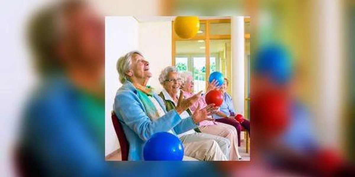groupe de femmes âgées heureux dans une salle de gym pour personnes âgées faisant des exercices de coordination de la main jeter et attraper des boules de plastique aux couleurs vives comme ils sont assis dans leurs chaises