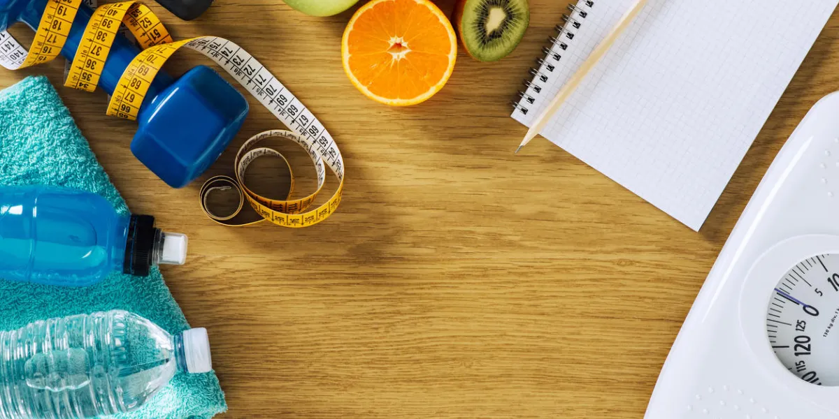 fitness and weight loss concept, dumbbells, white scale, notebook, tape measure and fruit on a wooden table, top view fitness and weight loss concept, dumbbells, white scale, notebook, tape measure and fruit on a wooden table, top view