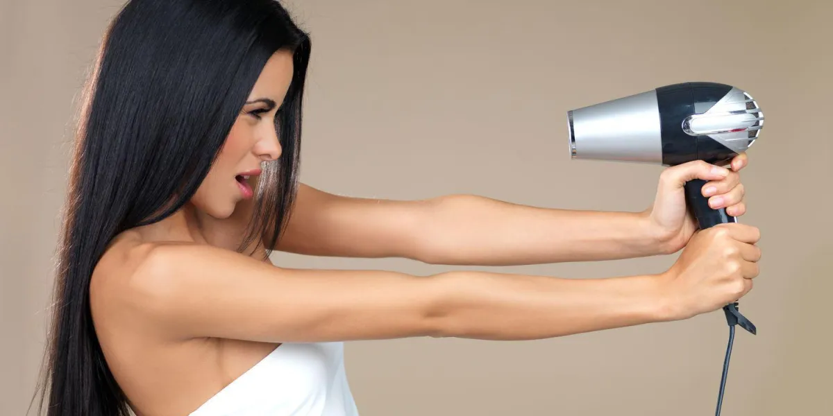 femme ludique s'amuser avec un sèche-cheveux en le tenant dans ses mains tendues pointant vers son propre visage isolé sur beige