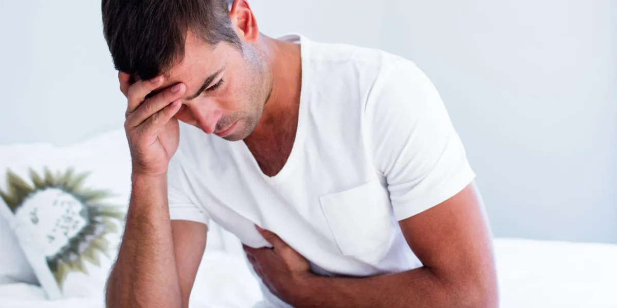jeune homme assis avec douleur à l'estomac sur le lit
