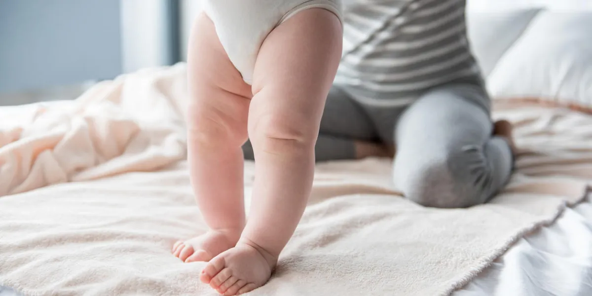close up of infant legs standing on bed, female sitting on background focus on feet