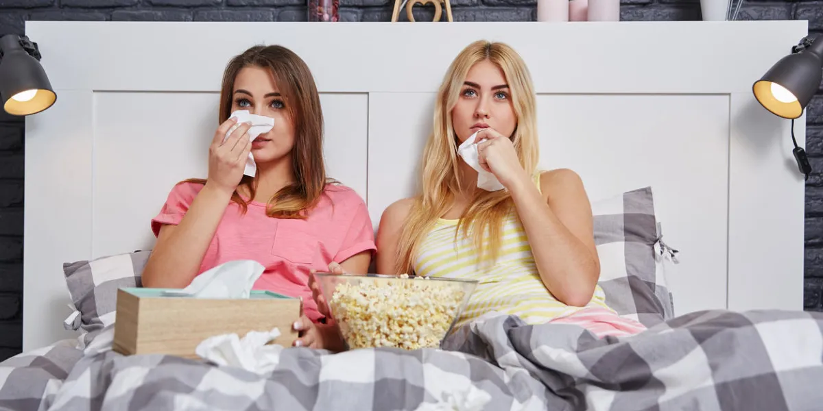 portrait of two friends in bed watching sad movie and crying