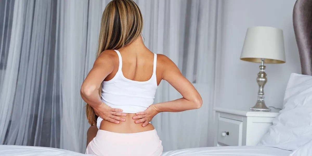 jeune femme assise sur le lit avec le mal de dos