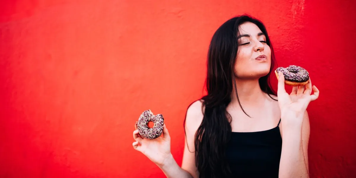 young happy caucasian girl eating chocolate donuts in front of red wall
